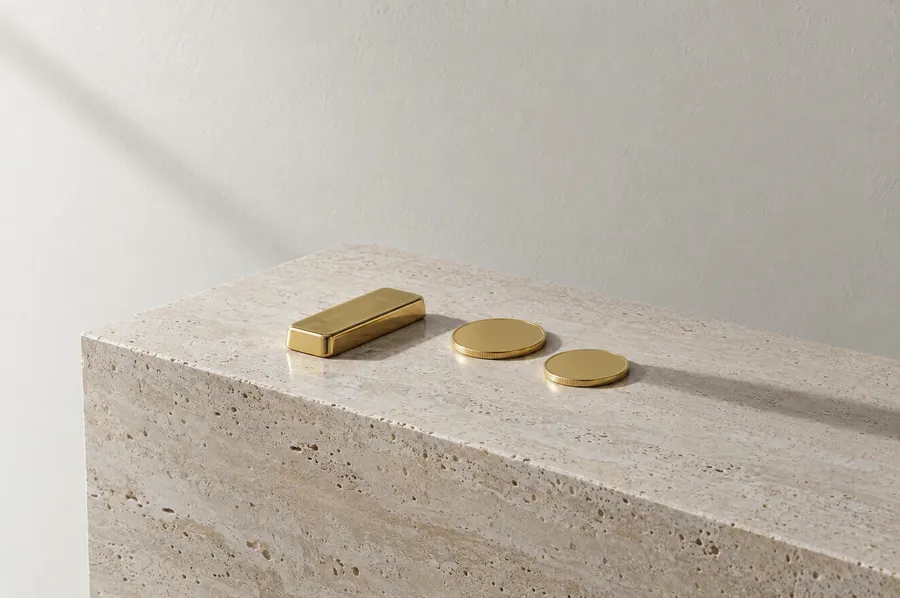 Ein glatter kleiner Goldbarren und zwei schlichte Goldmünzen auf einem Sockel aus hellem Travertin