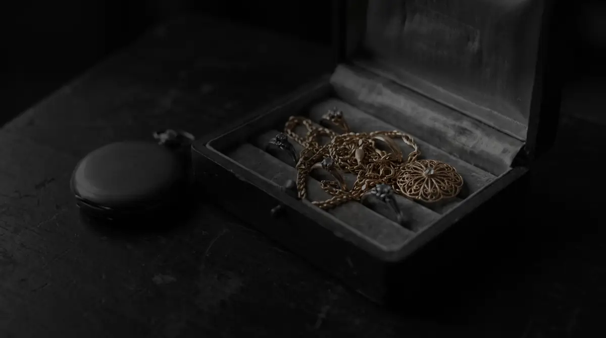 Eine geöffnete alte Schmuckschatulle mit Goldketten, Ringen und einer Filigranbrosche, daneben eine geschlossene Taschenuhr